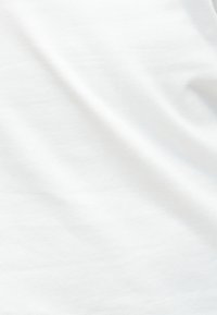 Gros plan sur un tissu blanc lisse avec des ombres subtiles et de légers plis indiquant une texture douce.