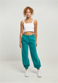 Teal joggebukser med elastiske mansjetter og liv, kombinert med en tettsittende hvit crop topp. Glatt stofftekstur, minimale designdetaljer.