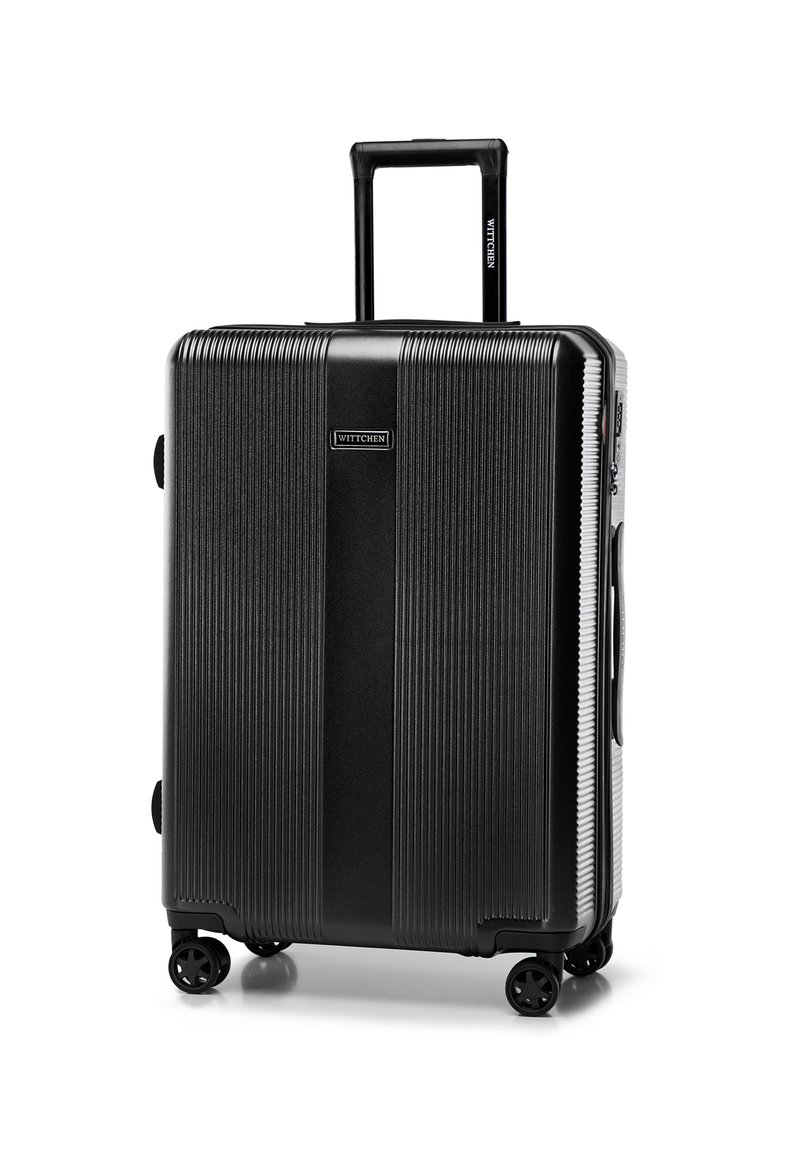 Maleta rígida negra con textura estriada, mango extensible, cuatro ruedas y un asa lateral. Presenta una placa con logo en la parte frontal.