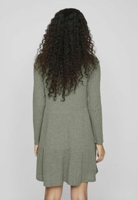 Robe à manches longues, en tissu côtelé, de couleur vert olive, avec un corsage ajusté et une jupe évasée à ourlet superposé pour une texture ajoutée.