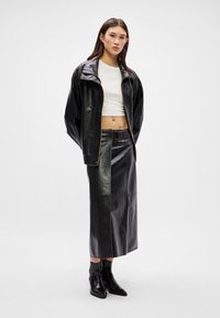 Μαύρα δερμάτινα μπουφάν με ψηλό γιακά, σε συνδυασμό με μια αντίστοιχη δερμάτινη μίνι φούστα. Λευκό crop top από κάτω. Μαύρες μποτάκια μέχρι τον αστράγαλο.