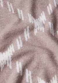 Pletená látka v jemně hnědé barvě s bílým abstraktním vzorem. Textura vypadá hladce a mírně elasticky, což ukazuje na útulný design.