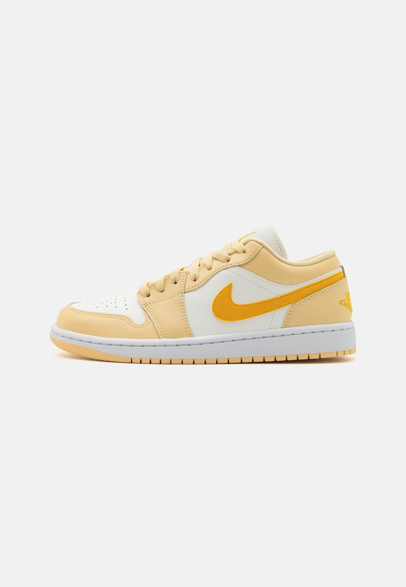 Baskets basses avec des panneaux beige et blanc, un swoosh Nike jaune, et une semelle blanche, présentées de côté extérieur sur un fond blanc.