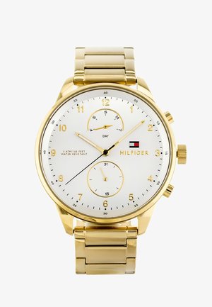 Montre-bracelet dorée avec un cadran blanc. Les caractéristiques incluent trois sous-cadrans pour le jour, la date et l'heure. Bracelet en acier inoxydable avec finition polie.