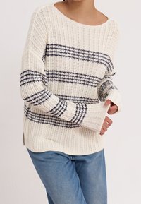 Randig stickad tröja i kräm och marinblå, med ribbad textur, bred halsringning och avslappnad passform med sidofåror vid nederkanten.