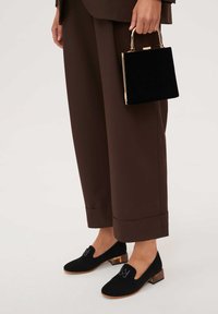 Czarne zamszowe buty na niskim słupku, z metaliczną emblematem. W zestawie z szerokimi brązowymi spodniami i czarną welwetową torebką.