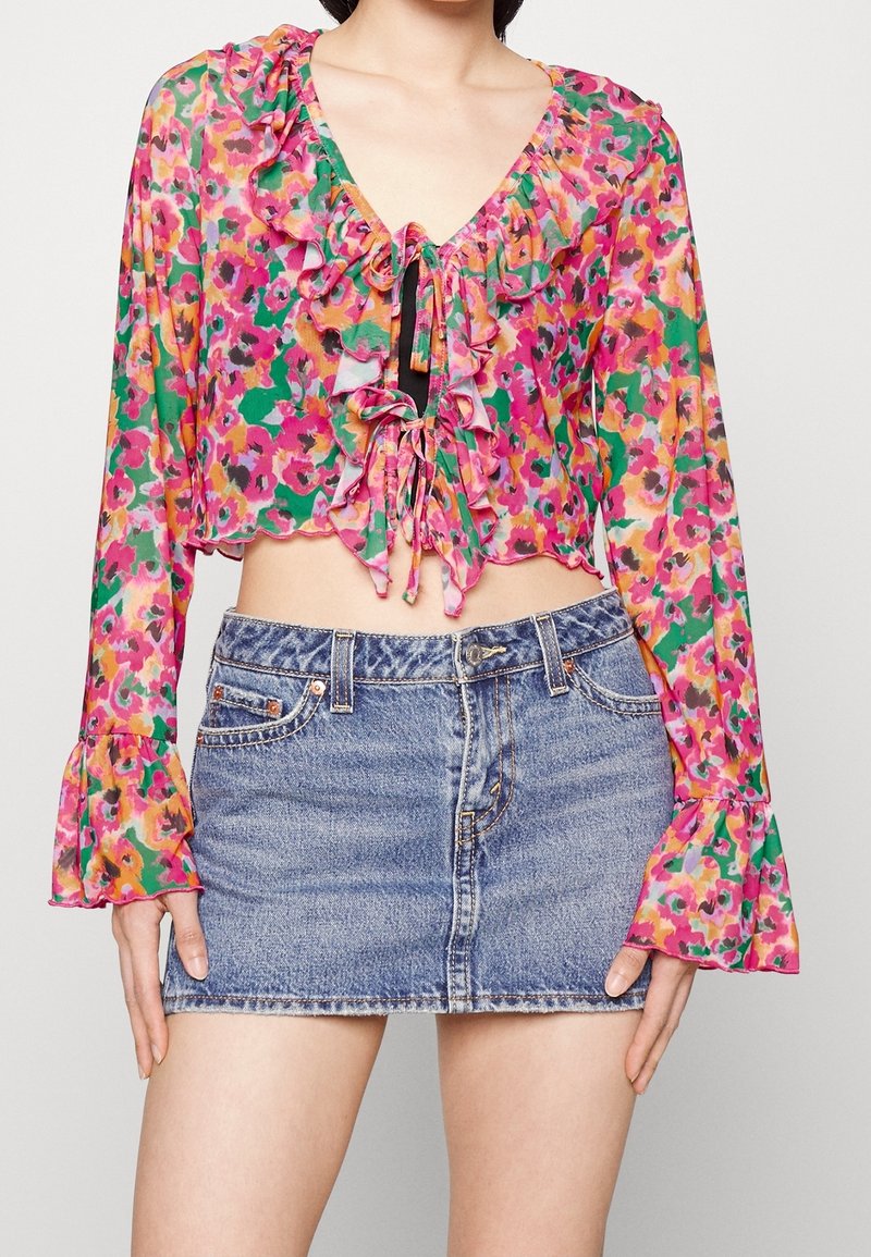 Blouse courte à imprimé floral en rose, vert et jaune avec des détails à volants ; associée à une mini-jupe en denim clair avec un ourlet effiloché.
