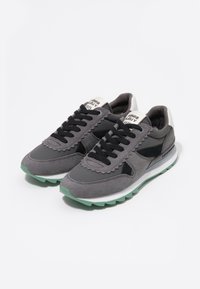 Graue Sportschuhe aus Wildleder und Stoff, mit einer gezackten Gestaltung, schwarzen Schnürsenkeln und einer grünen Gummisohle.