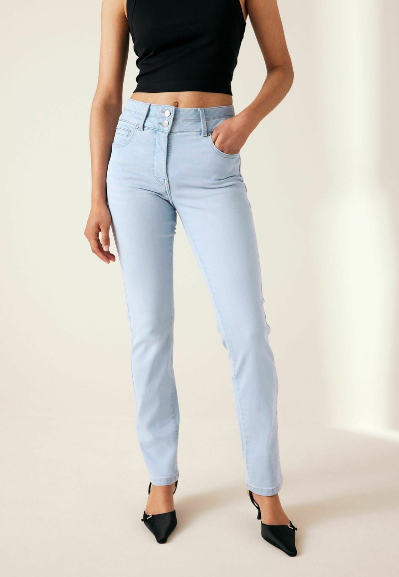 Jeans a vita alta di colore blu chiaro con chiusura a bottoni, gambe affusolate e tasche frontali, abbinati a tacchi a punta neri.