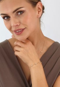 Goldschmuckset mit Ohrsteckern, einem Armband und einer Halskette mit floralen Akzenten, ausgestattet mit klaren Edelsteinen und zartem Kettendesign.