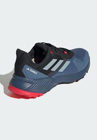 Czarnoszare buty sportowe z siateczkową cholewką, jasnoczerwonymi akcentami, trzema szarymi paskami, teksturowaną podeszwą i wzmocnionym projektem pięty.