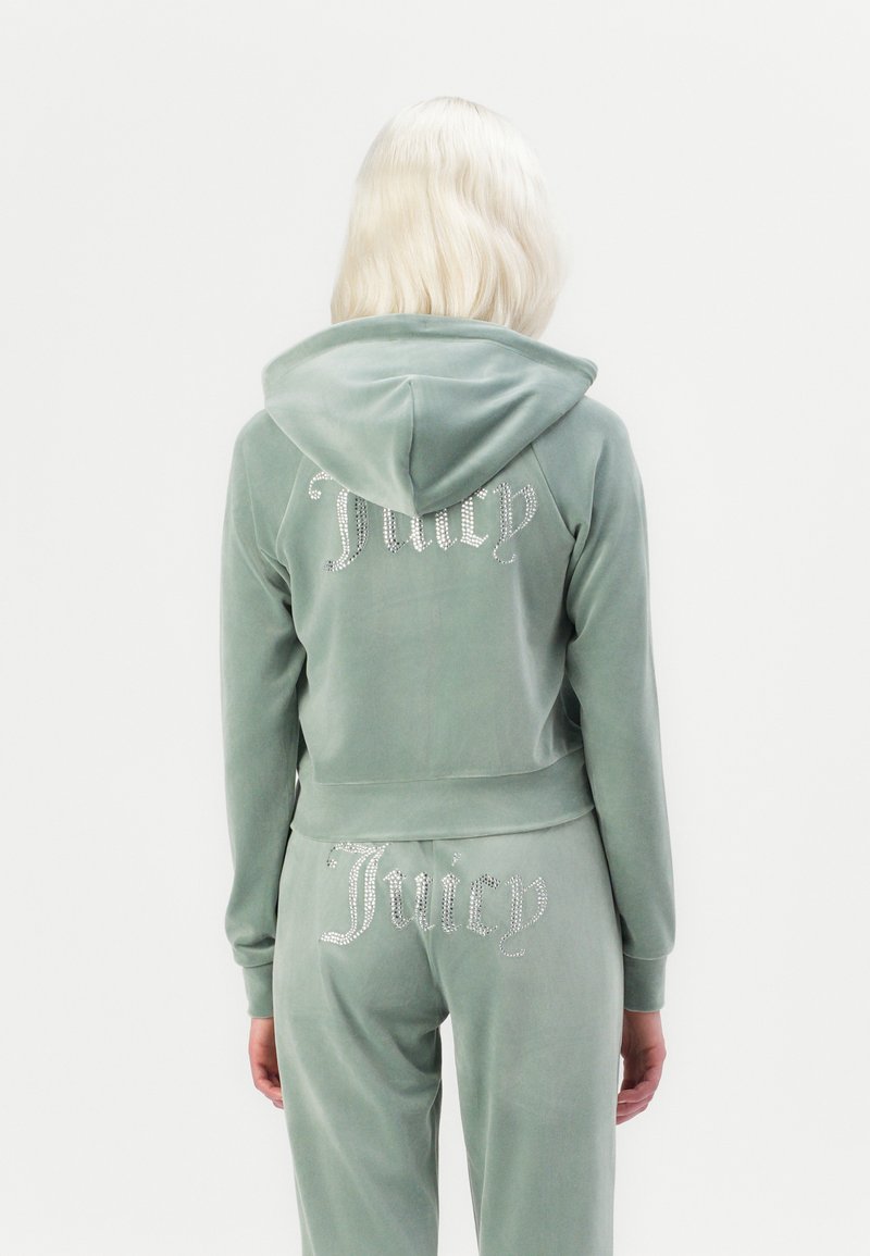 Velvet trainingspak in zachtgroen, met een cropped hoodie en joggingbroek. 'Juicy' is versierd met rhinestones op beide stukken.
