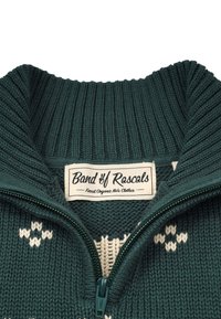 Grön stickad tröja med hög krage, dragkedja och vita geometriska mönster. Etiketten visar "Band of Rascals" med indikering av ekologisk bomull.