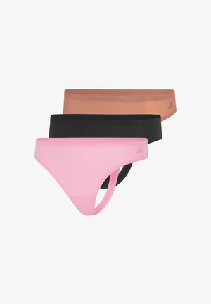 Vrouw staat op blote voeten, draagt een lichtroze sportbeha en bijpassende bikini-onderbroek tegen een effen witte achtergrond.