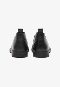 Botas tobilleras de cuero negro con acabado texturizado, punta redondeada y suela de goma. Lengüetas cortas en la parte posterior para facilitar su puesta.
