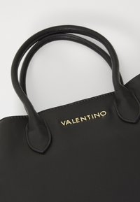 Crna kožna torba s dva čvrsta drška i zlatnim "Valentino" logotipom. Ima glatku teksturu i minimalistički dizajn.