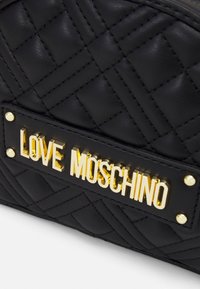 Black quilted leather surface with a gold metal "LOVE MOSCHINO" logo plaque attached by four gold studs.