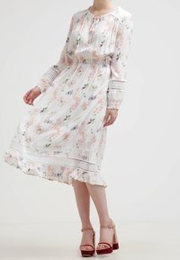 Vestido blanco con estampado floral en tonos pastel, mangas largas con detalles de encaje, cintura fruncida y dobladillo con volantes. Combinado con tacones rosa claro.