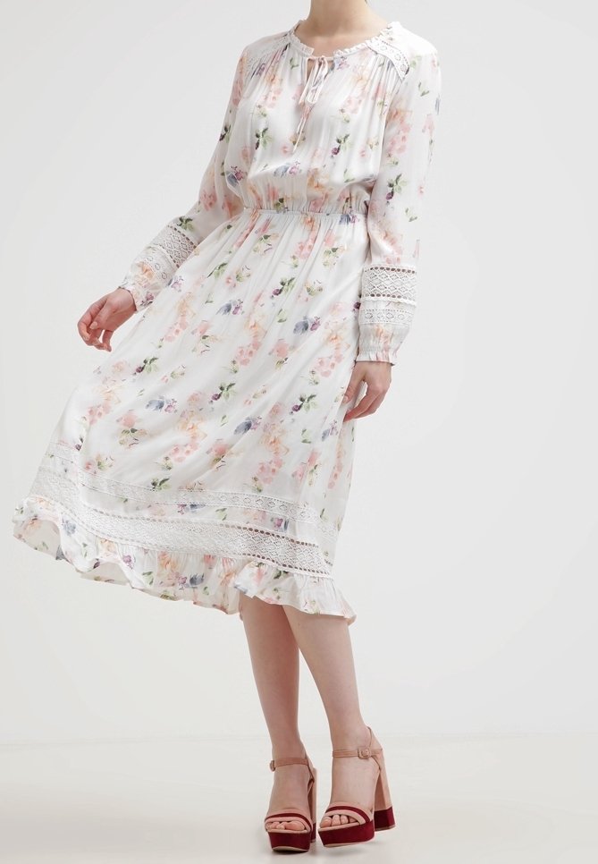 Vestido blanco con estampado floral en tonos pastel, mangas largas con detalles de encaje, cintura fruncida y dobladillo con volantes. Combinado con tacones rosa claro.