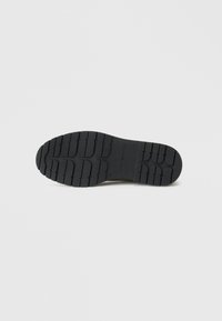 Semelle en caoutchouc noir avec un relief texturé et un motif de semelle pour une meilleure traction. Marquage et détails de taille estampés près du talon.