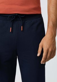 Marineblauwe katoenen joggingbroeken met een elastische tailleband en een trekkoord met oranje uiteinden. Gladde textuur en taps toelopende pasvorm.