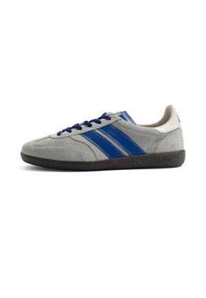 Szary zamszowy sneaker z niebieskimi paskami, niebieskimi sznurówkami, białą nasadką na pięcie i czarną teksturowaną podeszwą, pokazany z profilu.