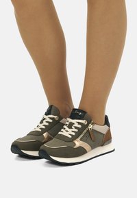 Grüne Sportschuhe aus strukturiertem Stoff, mit goldenen Akzenten, weißen Schnürsenkeln und einem seitlichen Reißverschluss. Entworfen mit einer kontrastierenden braunen Ferse.