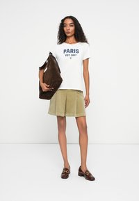 White t-shirt with blue "PARIS EST. 2007" print, khaki corduroy skirt, brown suede bag, and brown loafers with gold hardware accents.