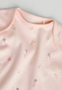 Minkštas rožinis medvilninis kūdikio kombinezonas su apvalia iškirpte, puoštas fėjų ir gėlių raštais. Lygus audinys ir elastinga apdaila palei kraštus.