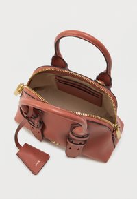 Καφέ δερμάτινη τσάντα με διπλές κοντές λαβές, χρυσό φερμουάρ, εσωτερικές τσέπες και ετικέτα. Διαθέτει λεία υφή και δομημένο σχήμα.