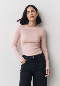 Long-sleeve, ribbed light pink top with a round neckline, paired with high-waisted black jeans. The fabric appears soft and fitted.