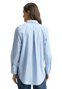 Light blue striped shirt with a back pleat, long sleeves, and buttoned cuffs. Features subtle decorative dots on fabric.