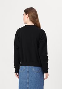 Felpa nera con colletto a girocollo, vestibilità ampia e polsini a costine, abbinata a una gonna di jeans, vista dal retro.