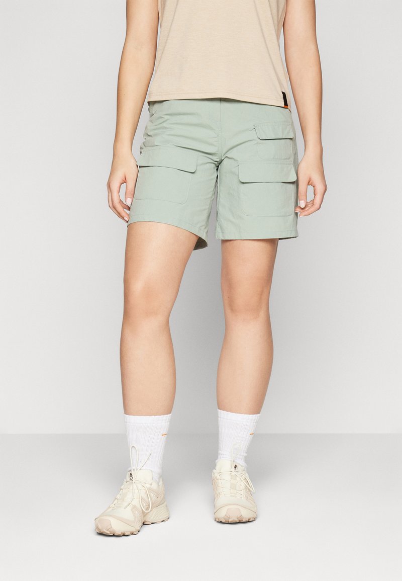 Cargo shorts i lys grønn stoff, med to store frontlommer og en avslappet passform. Kombinert med en beige topp og lyse joggesko.