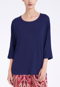 Top blu navy a maniche lunghe con scollatura rotonda. Tessuto morbido con vestibilità comoda, abbinato a pantaloni rossi con motivo.
