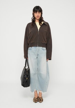 Brązowa krótka kurtka na zamek, jasnooliwkowa koszula, wyblakłe niebieskie szerokie dżinsy z postrzępionymi brzegami, czarna torebka i czółenka w cętki lamparta.