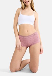 Pantaloni corti hipster rosa realizzati in un morbido tessuto con un motivo nero ondulato, dotati di una cintura decorativa. Abbinati a un top corto bianco.
