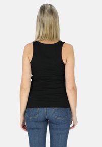 Canottiera nera con costine e spalline larghe, caratterizzata da un design aderente e una texture liscia, abbinata a jeans in denim blu.