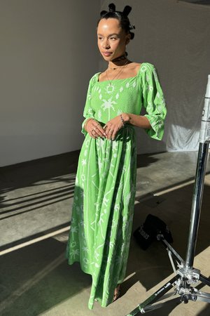 Lungo abito verde realizzato in tessuto testurizzato, con motivi botanici bianchi e maniche a sbuffo. L'abito presenta un corpetto aderente e una gonna fluida.