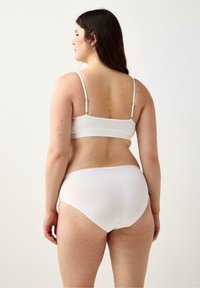 Valkoinen puuvillainen bralette ohuilla olkaimilla, yhdistettynä valkoisiin korkeavyötäröisiin pikkuhousuihin. Sileä rakenne, yksinkertainen muotoilu, ei näkyviä kuvioita tai varusteita.