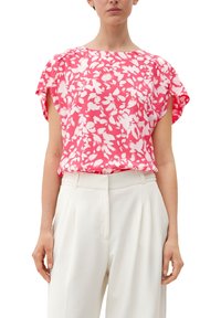 Blumenmuster in Rosa Bluse mit kurzen, fließenden Ärmeln, aus einem weichen, leichten Stoff und mit lockerem Schnitt, kombiniert mit weiten weißen Hosen.