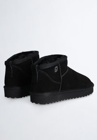 Botines de ante negro con punta redondeada, forro interior suave y suelas de goma texturizadas. Presentan un detalle de costura y una lengüeta en la parte trasera.