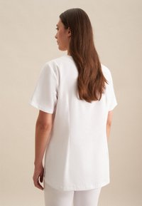 Top bianco a maniche corte con taglio dritto, realizzato in tessuto morbido, con spacco laterale e scollatura a girocollo.