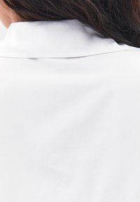 Weißes Hemd mit Kragen, glatte Textur, schlichtes Design, Rückansicht, die die Nähte am Kragen und den Stofffall zeigt.