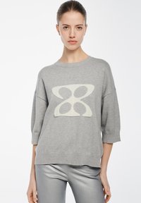 Grauer Pullover mit einem großen cremefarbenen abstrakten Muster auf der Vorderseite, mit rundem Ausschnitt und Dreiviertelärmeln, gefertigt aus einem weichen Material.