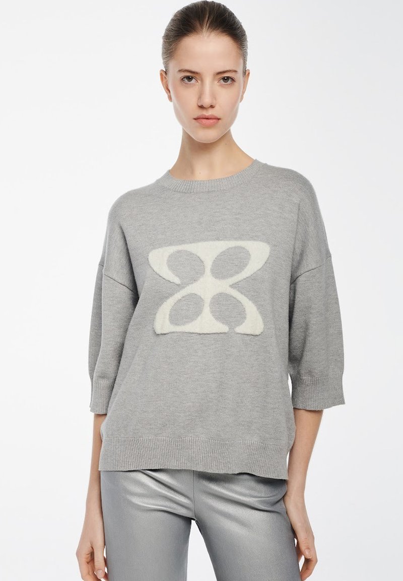 Grauer Pullover mit einem großen cremefarbenen abstrakten Muster auf der Vorderseite, mit rundem Ausschnitt und Dreiviertelärmeln, gefertigt aus einem weichen Material.