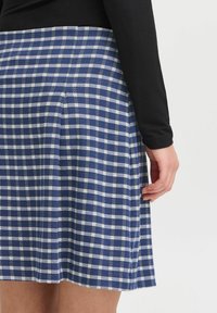 Jupe à carreaux bleus et blancs avec des plis, faite de tissu, présente une texture lisse et une taille s'harmonisant avec un haut à manches longues noir.