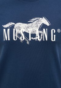 Námořnický modrý tričko vyrobené z bavlny s kulatým výstřihem. Obsahuje bílou grafiku běžícího koně a slovo "MUSTANG" tučným písmem.