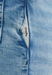 Jeans in denim azzurro chiaro con una texture invecchiata, caratterizzati da un'etichetta bianca cucita nella cucitura laterale con la scritta "CHASIN'."