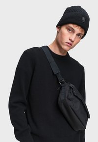 Čierna pletená čiapka, priliehavá. Čierny sveter, s okrúhlym výstrihom. Čierna crossbody taška, obdĺžnikový tvar, textúrovaná látka, nastaviteľný popruh.